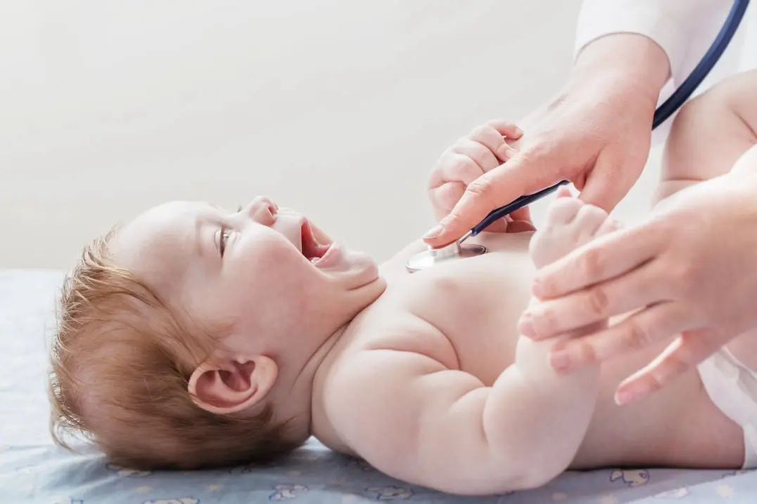 Bebê sorrindo enquanto o médico coloca o estetoscópio no seu peito